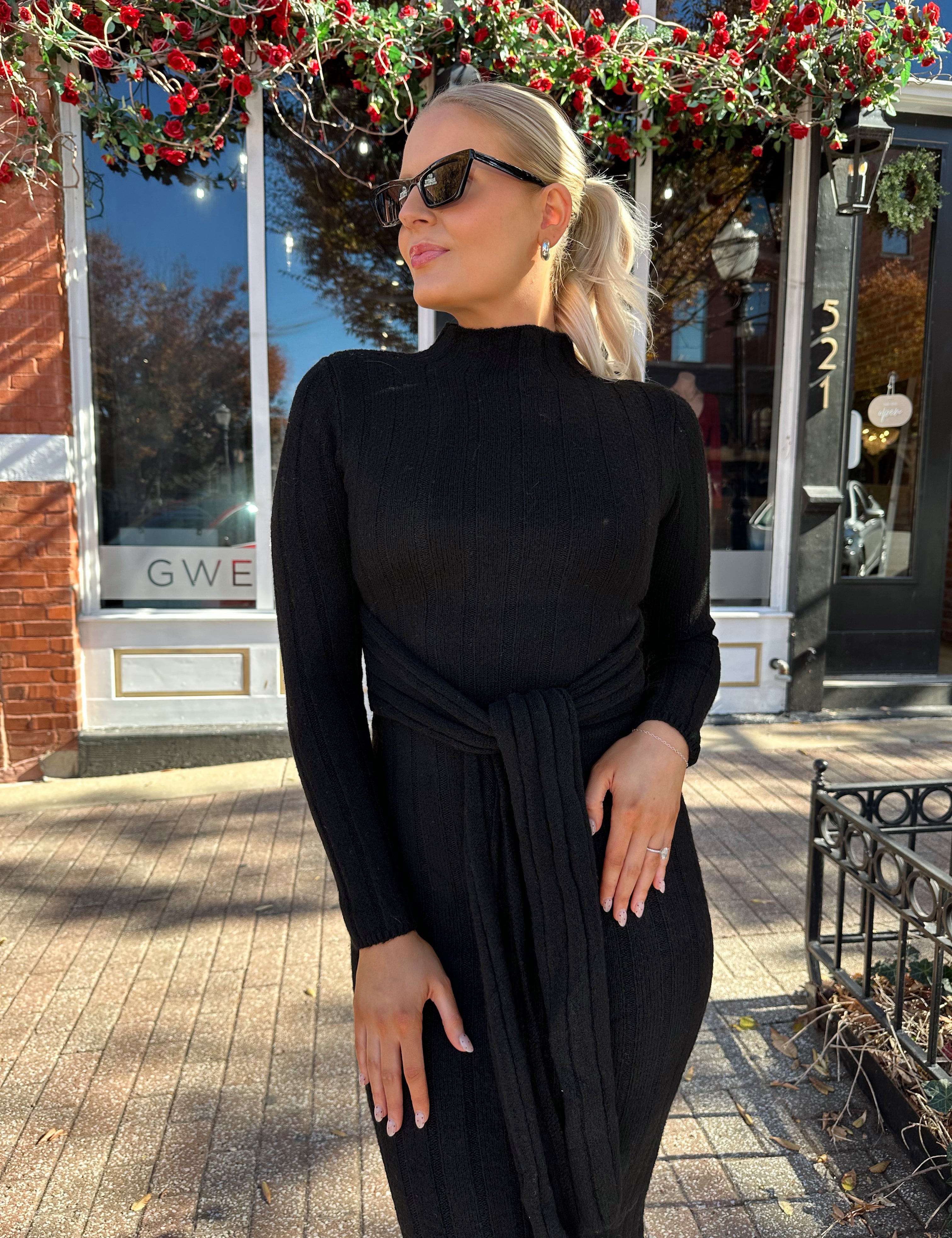 Woman wearing black knit sweater midi dress with front tie detail. 