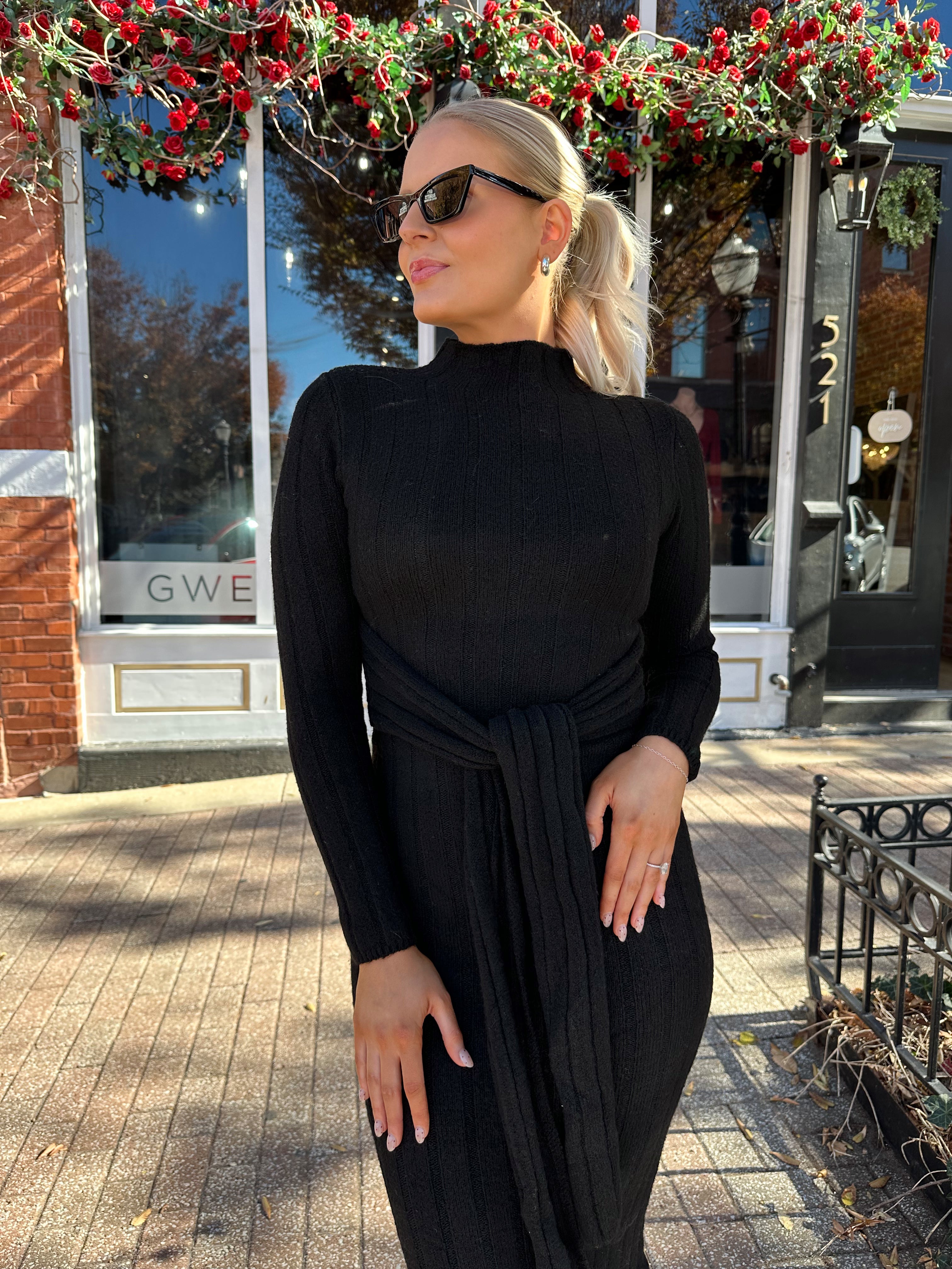 Woman wearing black knit sweater midi dress with front tie detail. 