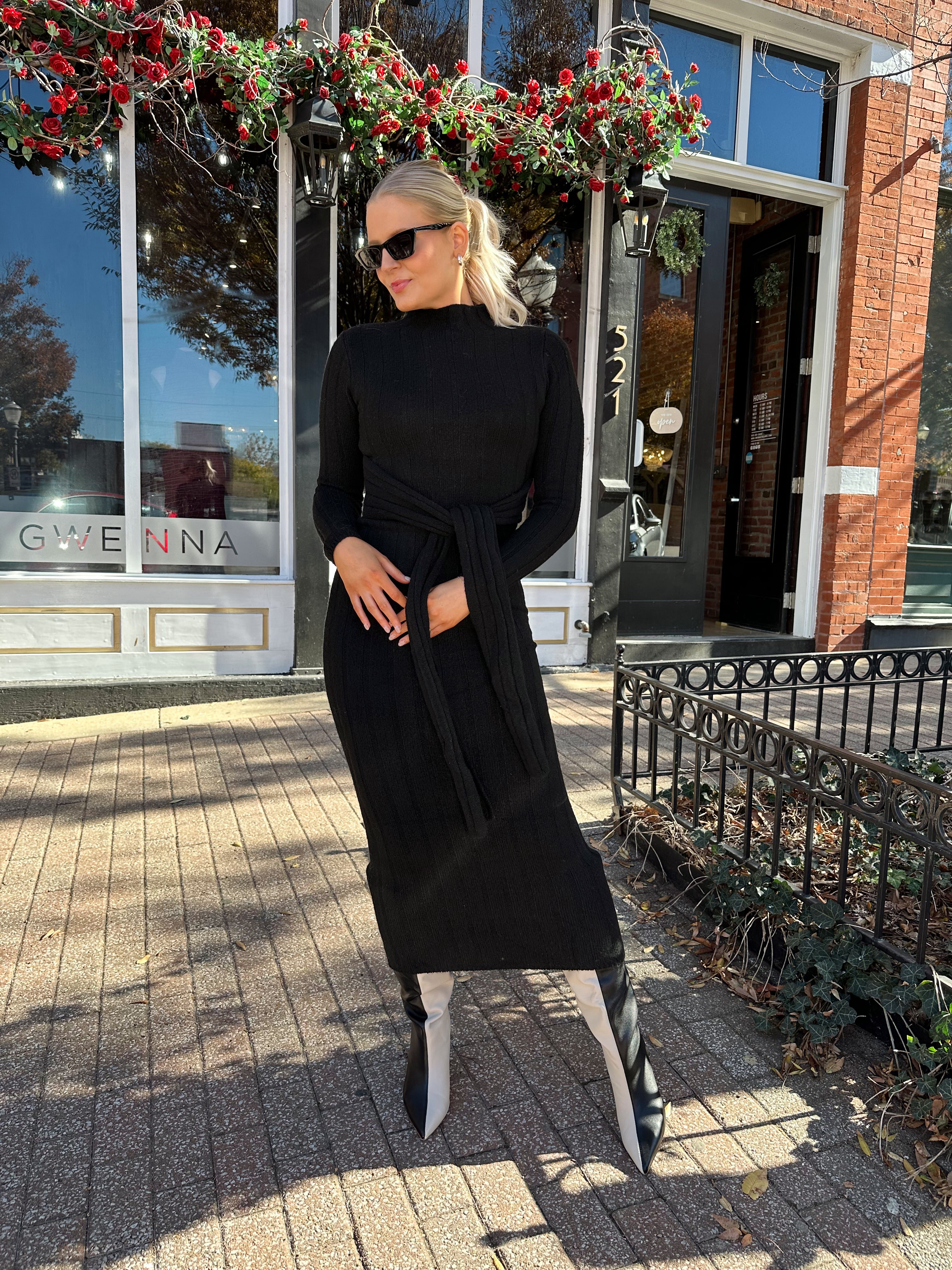 Woman wearing black knit sweater midi dress with front tie detail. 