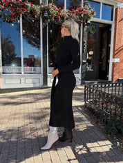 Woman wearing black knit sweater midi dress with front tie detail. 