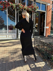 Woman wearing black knit sweater midi dress with front tie detail. 