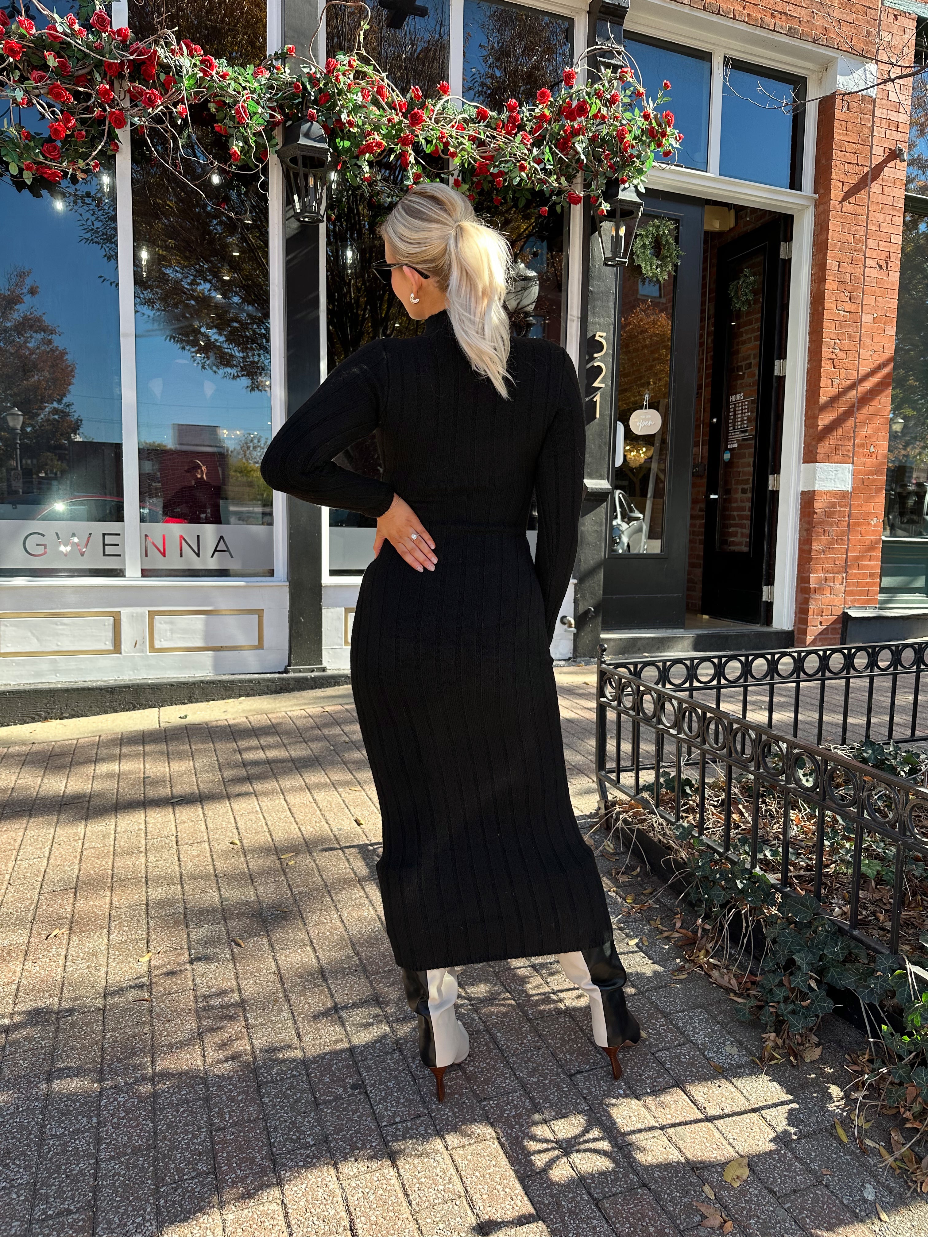 Woman wearing black knit sweater midi dress with front tie detail. 