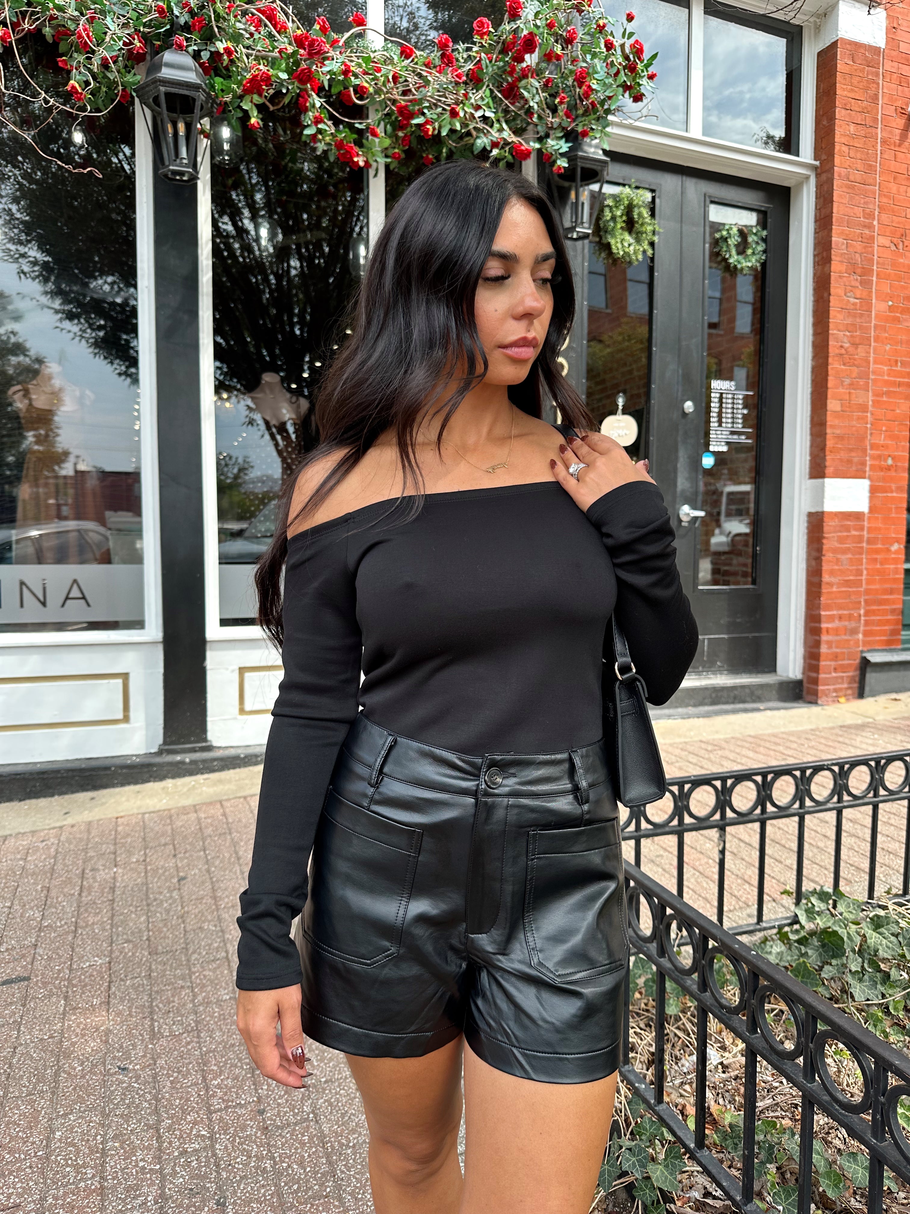 Woman wearing black off the shoulder long sleeve off the shoulder top with black leather shorts.