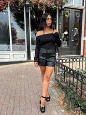 Woman wearing black off the shoulder long sleeve off the shoulder top with black leather shorts.