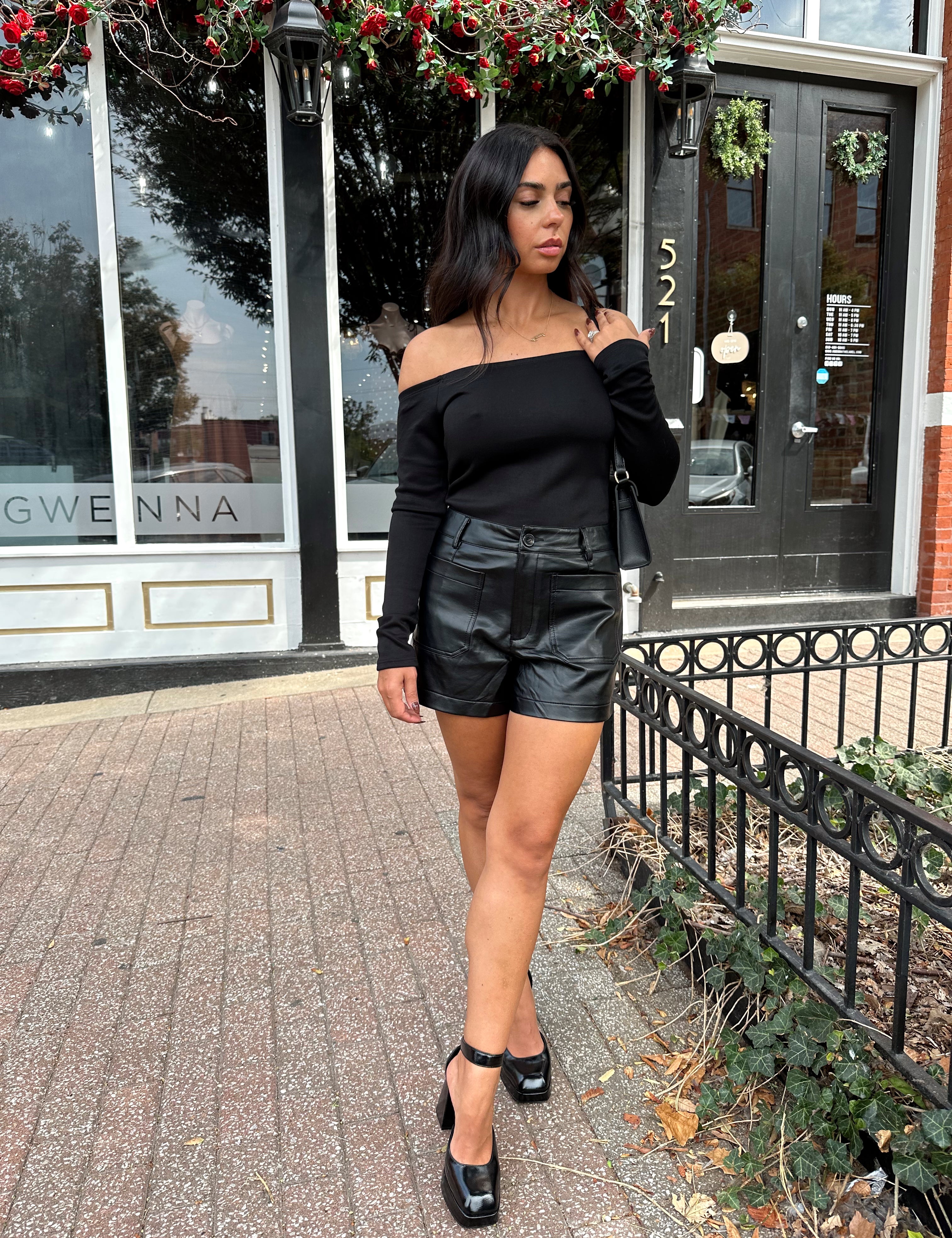 Woman wearing black off the shoulder long sleeve off the shoulder top with black leather shorts.