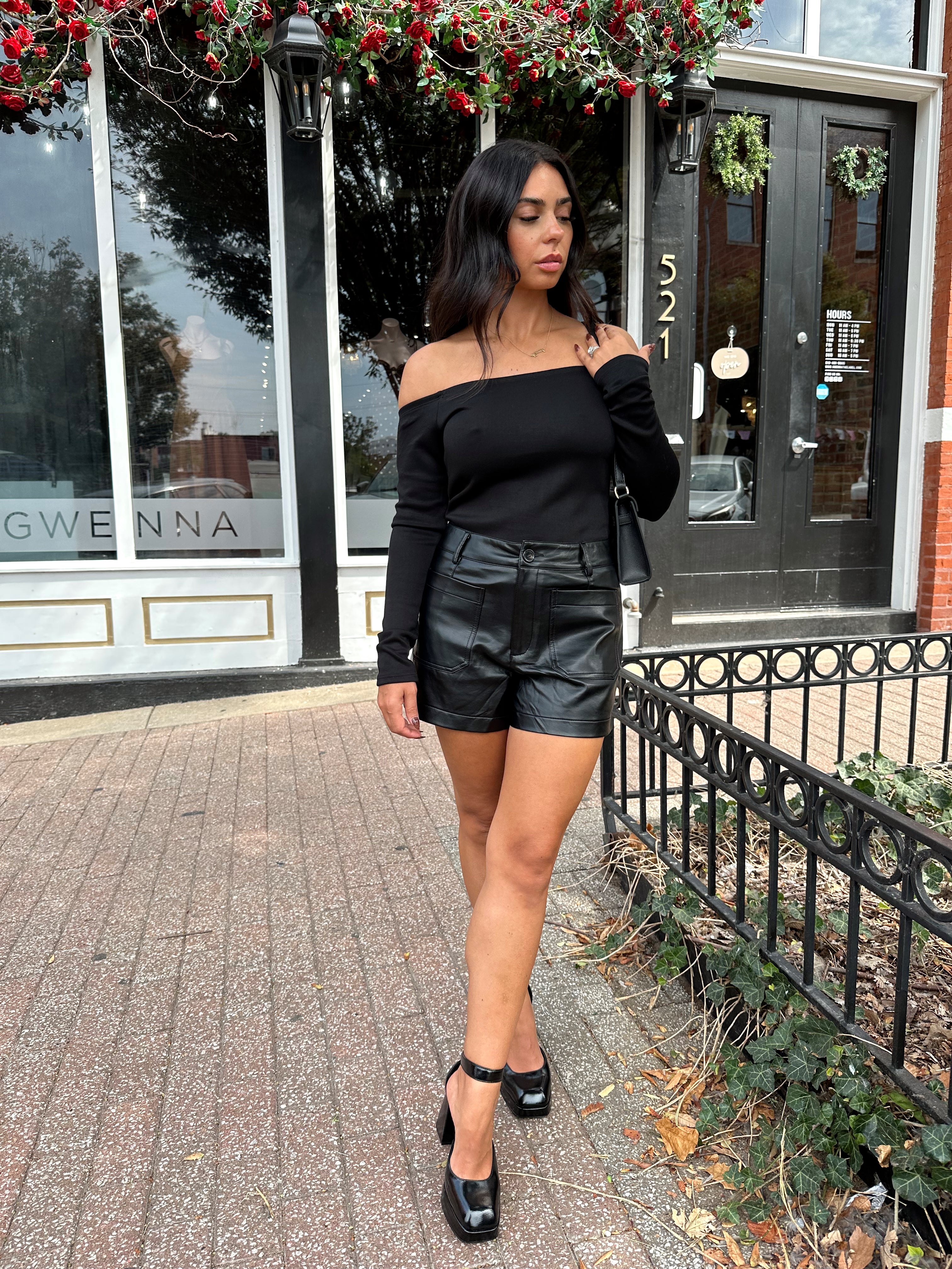 Woman wearing black off the shoulder long sleeve off the shoulder top with black leather shorts.