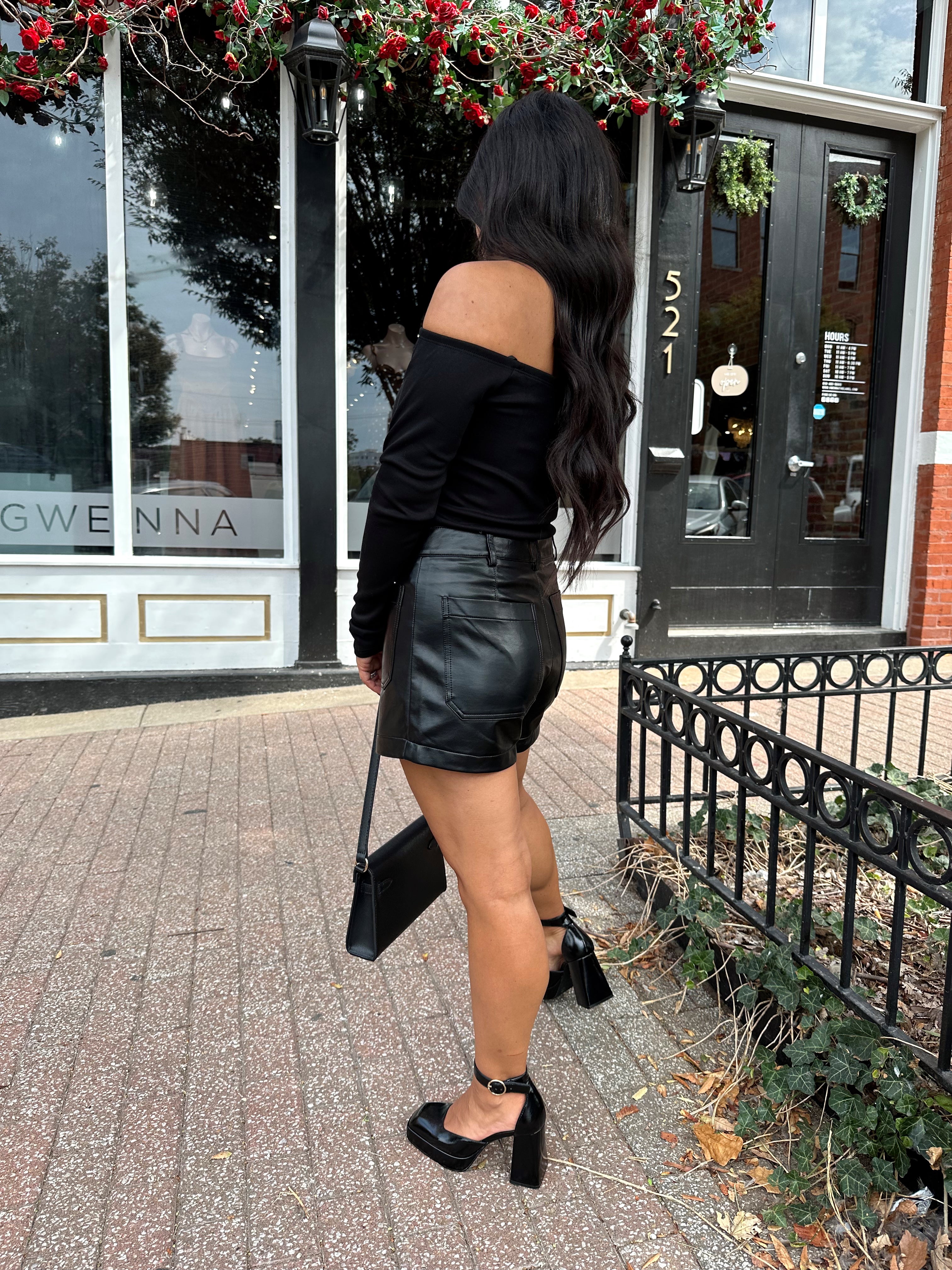 Woman wearing black off the shoulder long sleeve off the shoulder top with black leather shorts.