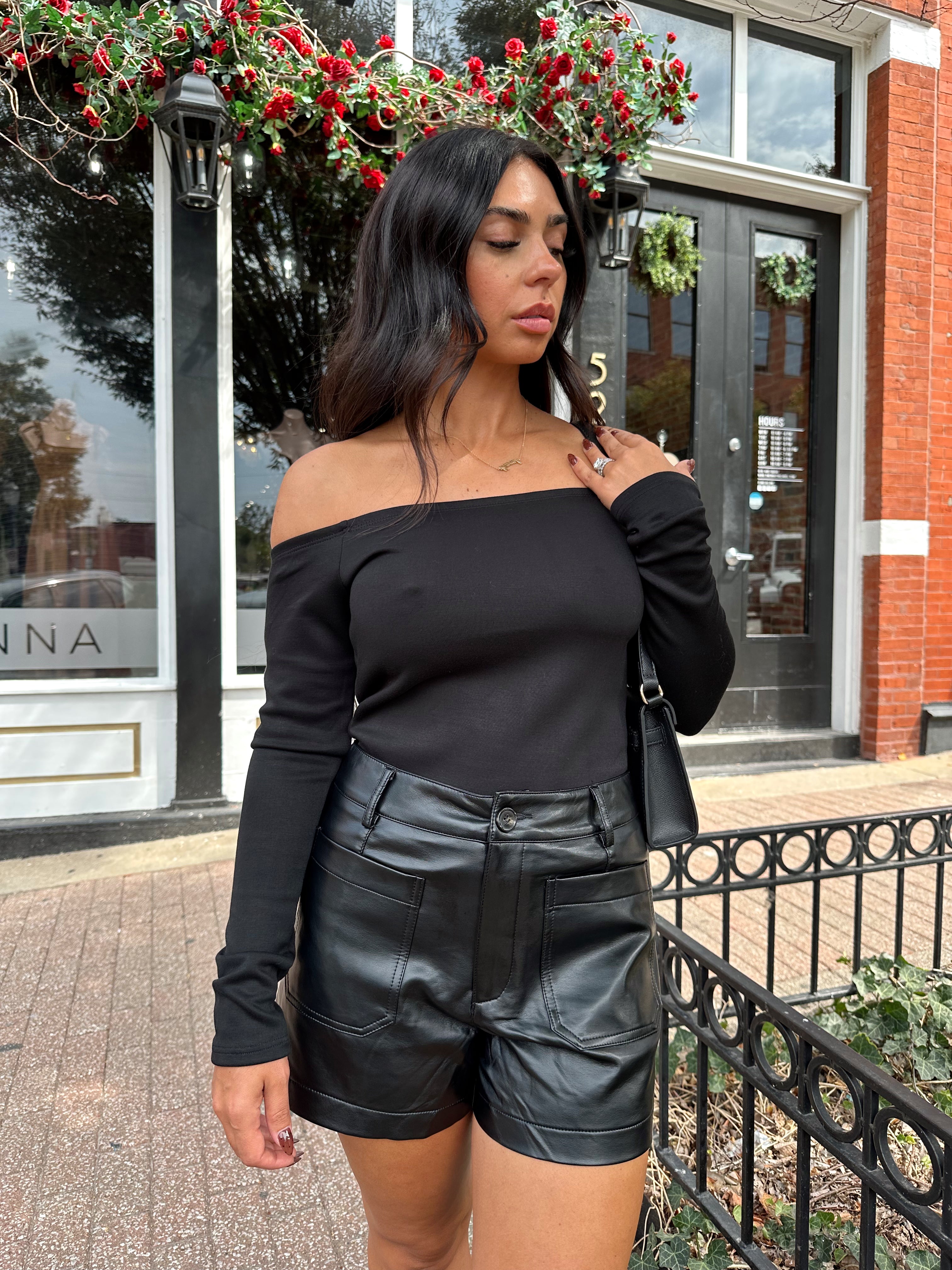Woman wearing black off the shoulder long sleeve off the shoulder top with black leather shorts.