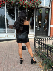 Woman wearing black off the shoulder long sleeve off the shoulder top with black leather shorts.