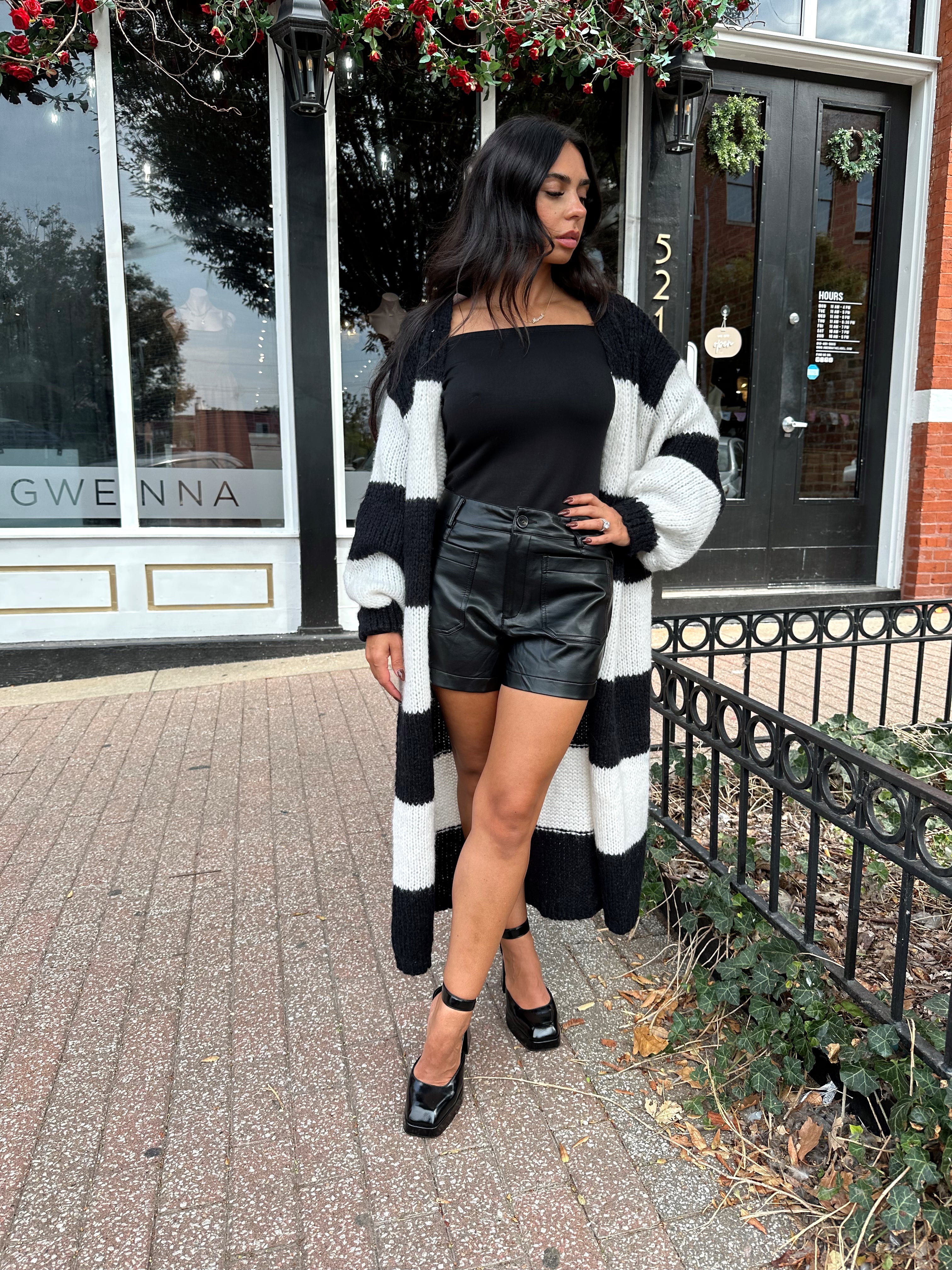 Woman wearing black off the shoulder long sleeve off the shoulder top with black leather shorts.