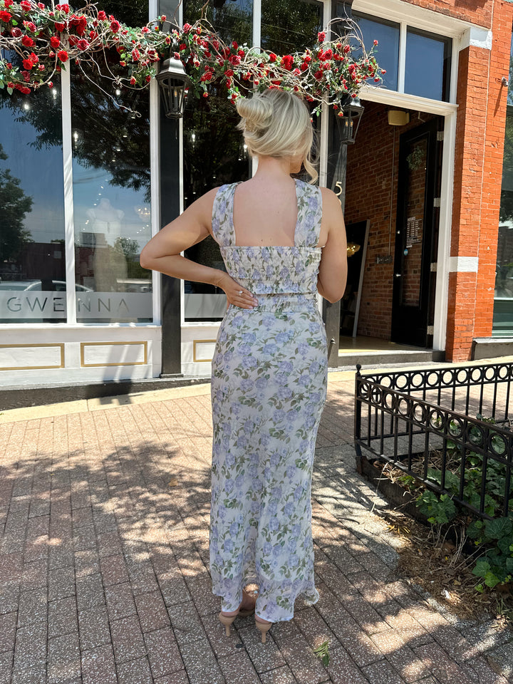 Woman wearing lilac floral two piece set with attachable neck scarf.