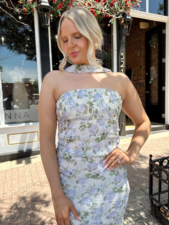 Woman wearing lilac floral two piece set with attachable neck scarf.