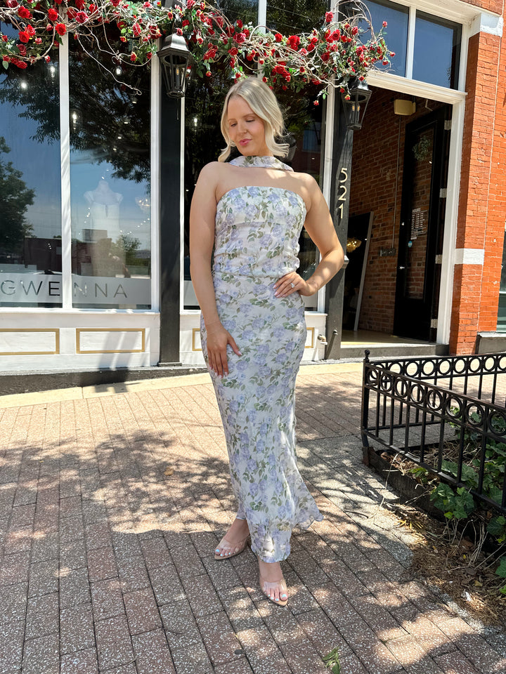 Woman wearing lilac floral two piece set with attachable neck scarf.