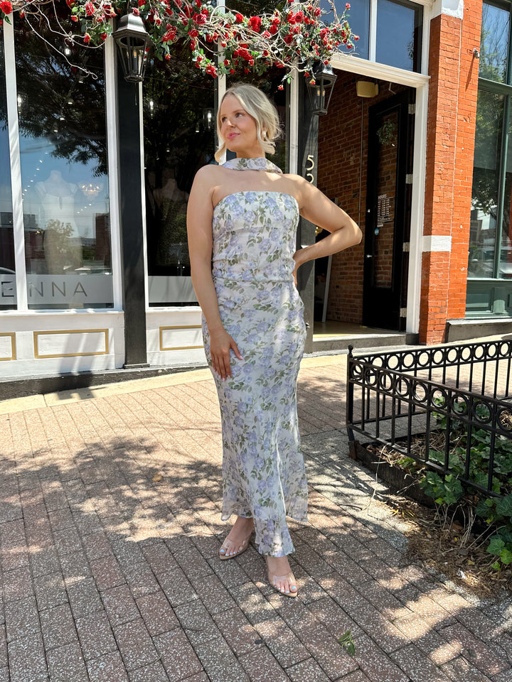 Woman wearing lilac floral two piece set with attachable neck scarf.