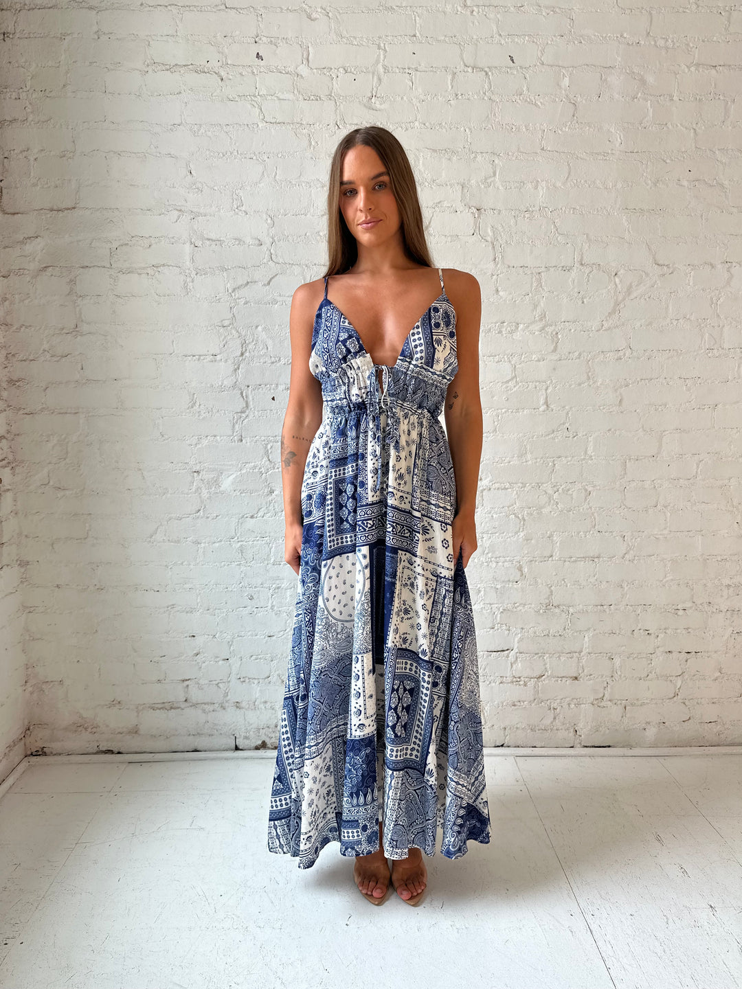 Woman wearing blue and white patchwork pattern midi dress with front tie detail.