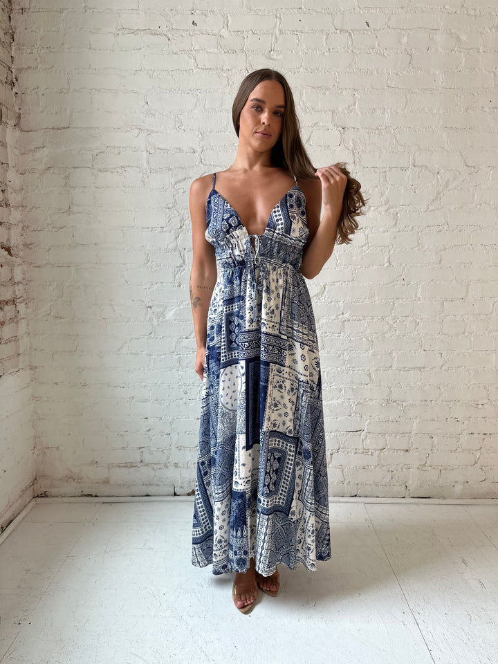 Woman wearing blue and white patchwork pattern midi dress with front tie detail.