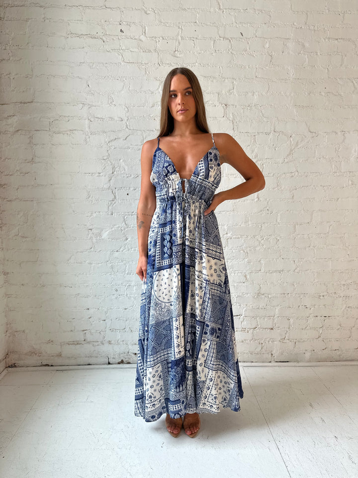 Woman wearing blue and white patchwork pattern midi dress with front tie detail.