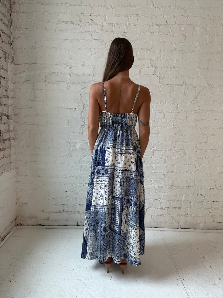 Woman wearing blue and white patchwork pattern midi dress with front tie detail.