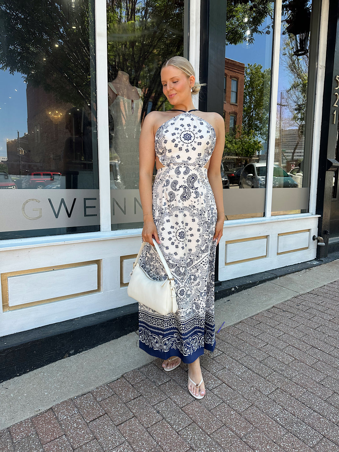 Woman wearing white and navy paisley print satin maxi dress with an open back and tie closure. 
