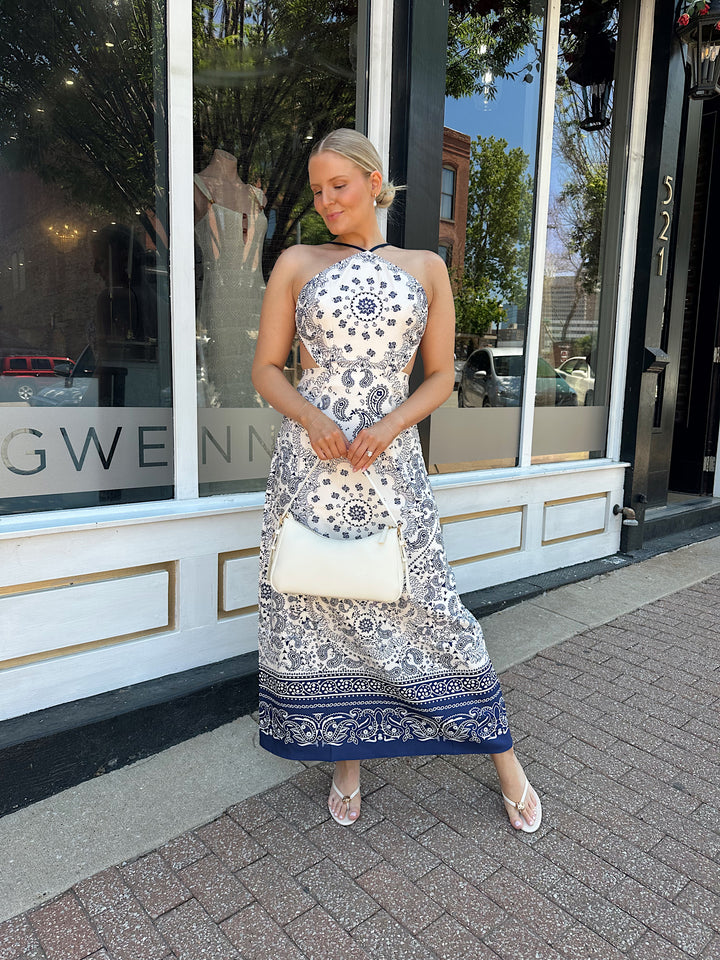 Woman wearing white and navy paisley print satin maxi dress with an open back and tie closure. 