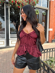 Woman wearing burgundy satin tank top with ruffle detail and leather shorts.