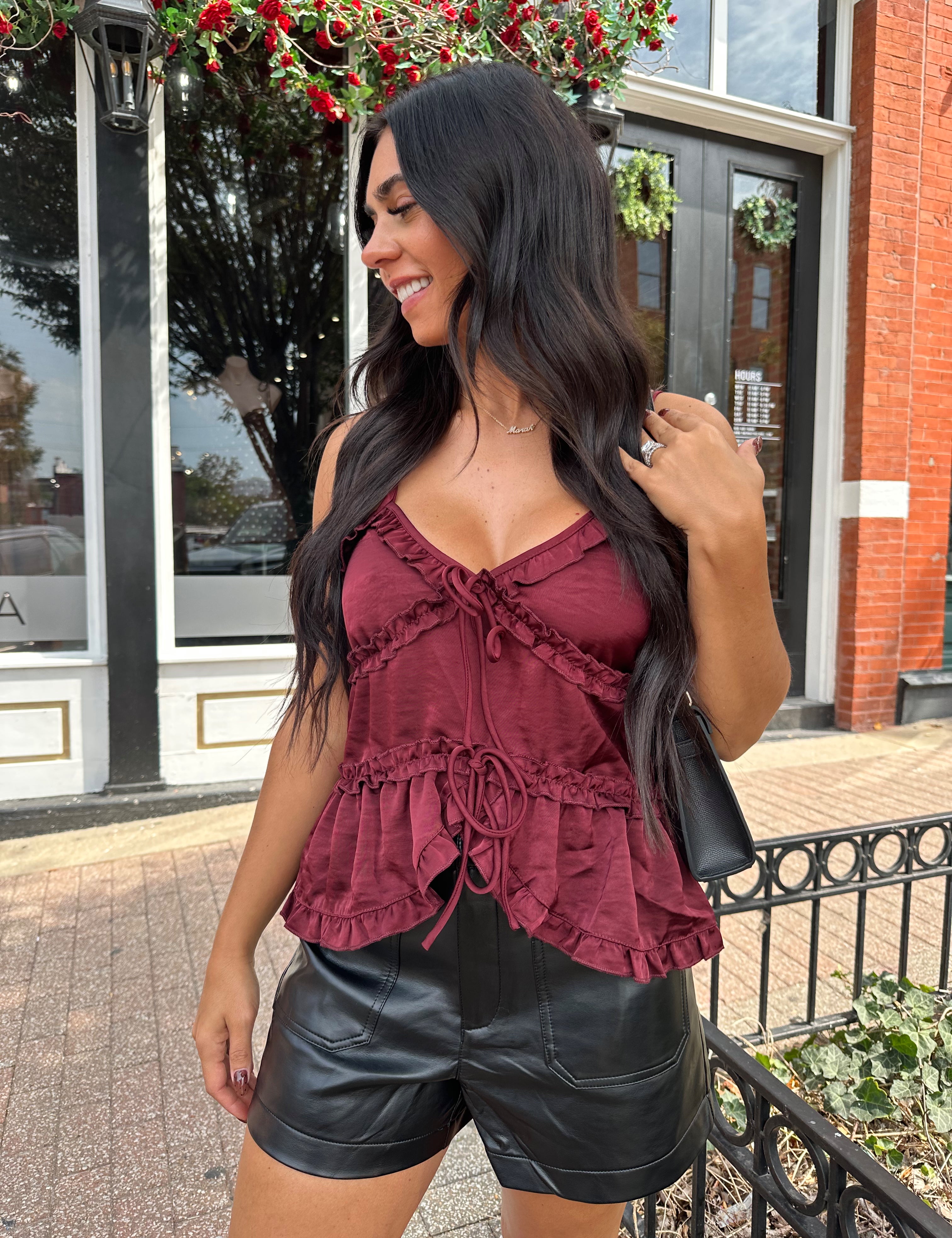 Woman wearing burgundy satin tank top with ruffle detail and leather shorts.