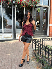 Woman wearing burgundy satin tank top with ruffle detail and leather shorts.