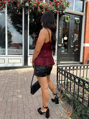 Woman wearing burgundy satin tank top with ruffle detail and leather shorts.