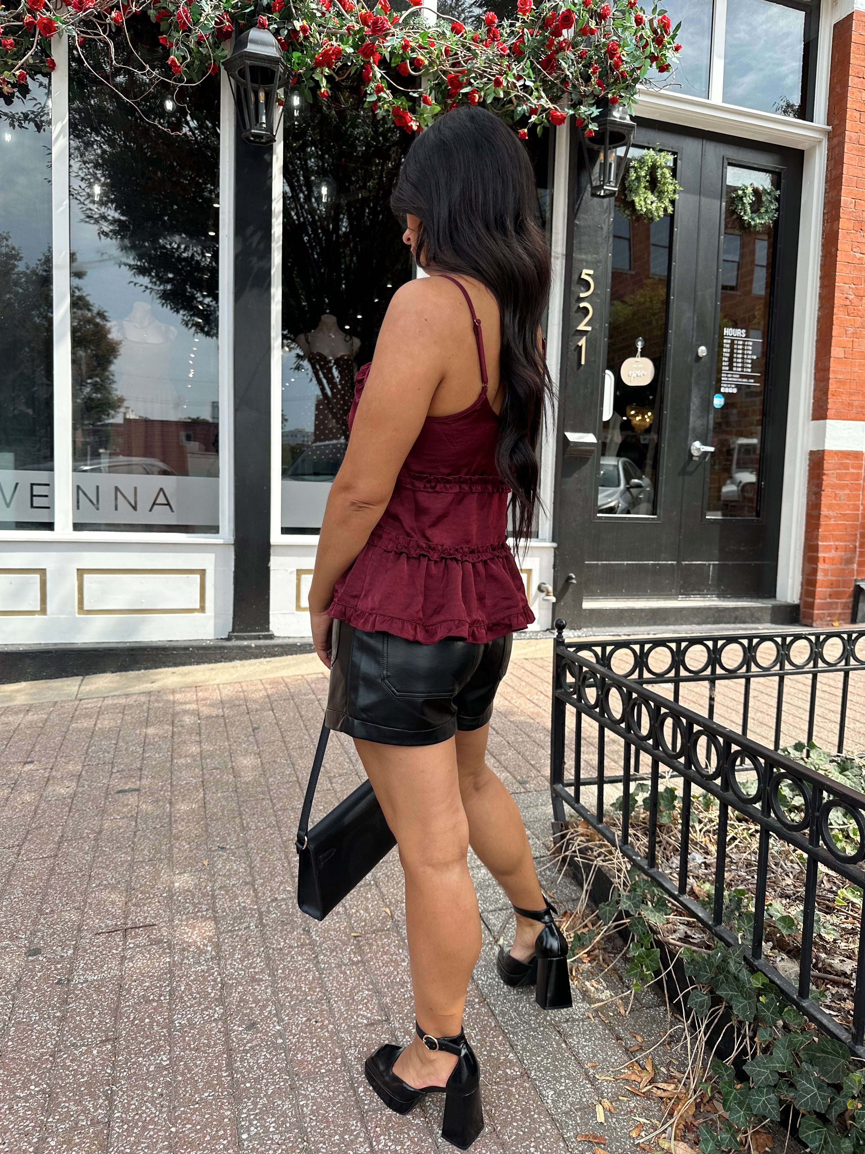 Woman wearing burgundy satin tank top with ruffle detail and leather shorts.