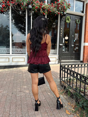 Woman wearing burgundy satin tank top with ruffle detail and leather shorts.