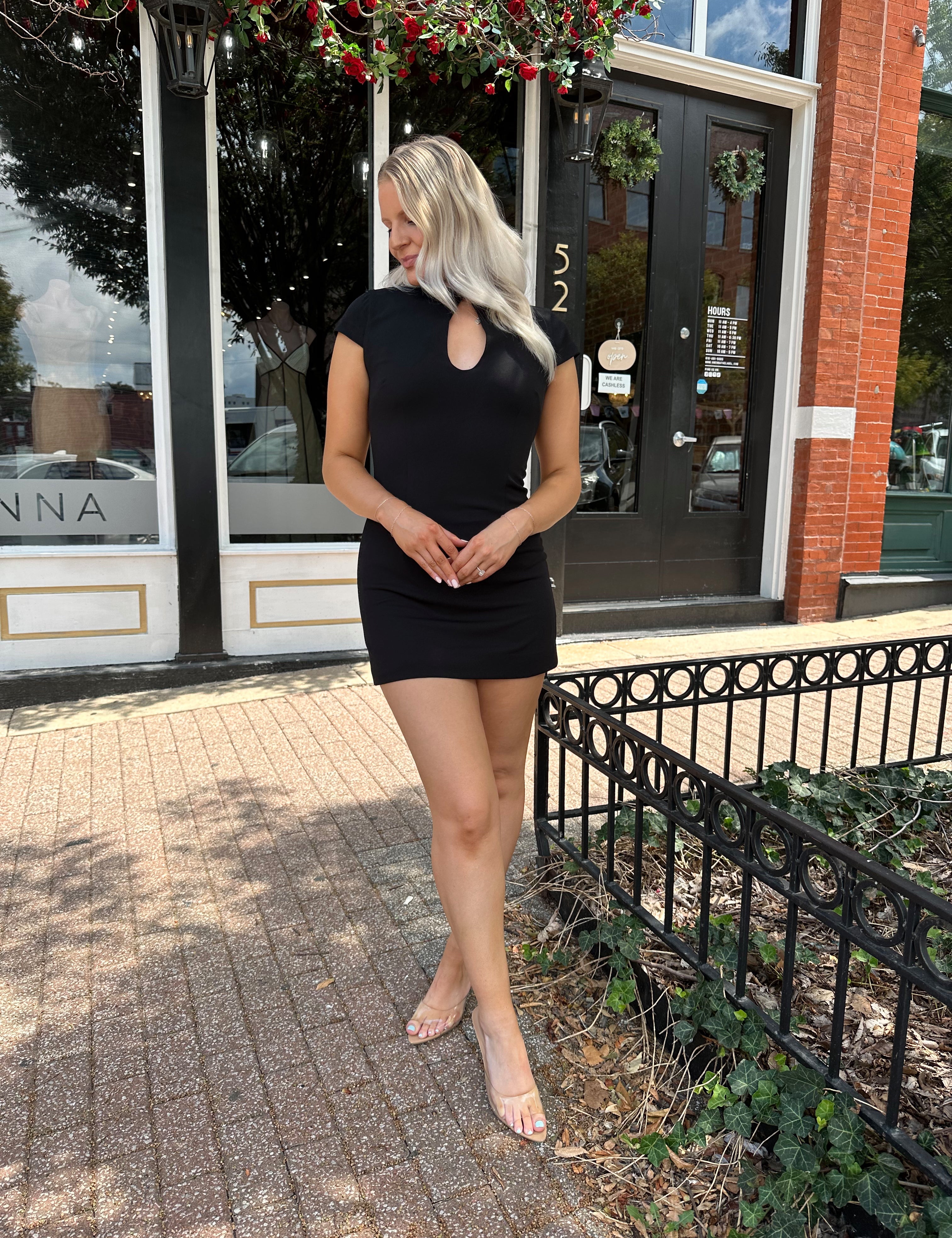 Woman wearing black tailored mini dress with short sleeves and keyhole cutout.