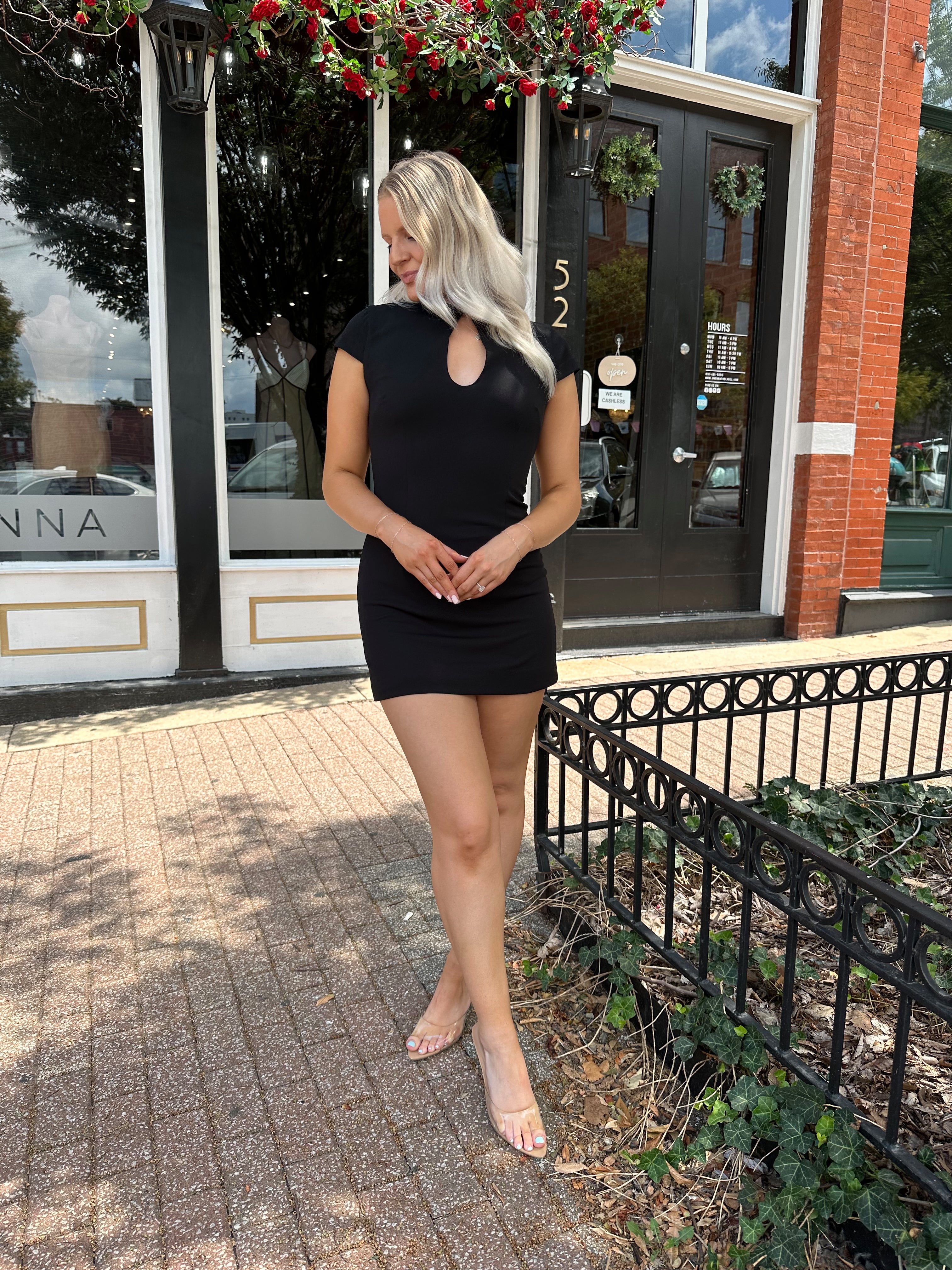 Woman wearing black tailored mini dress with short sleeves and keyhole cutout.