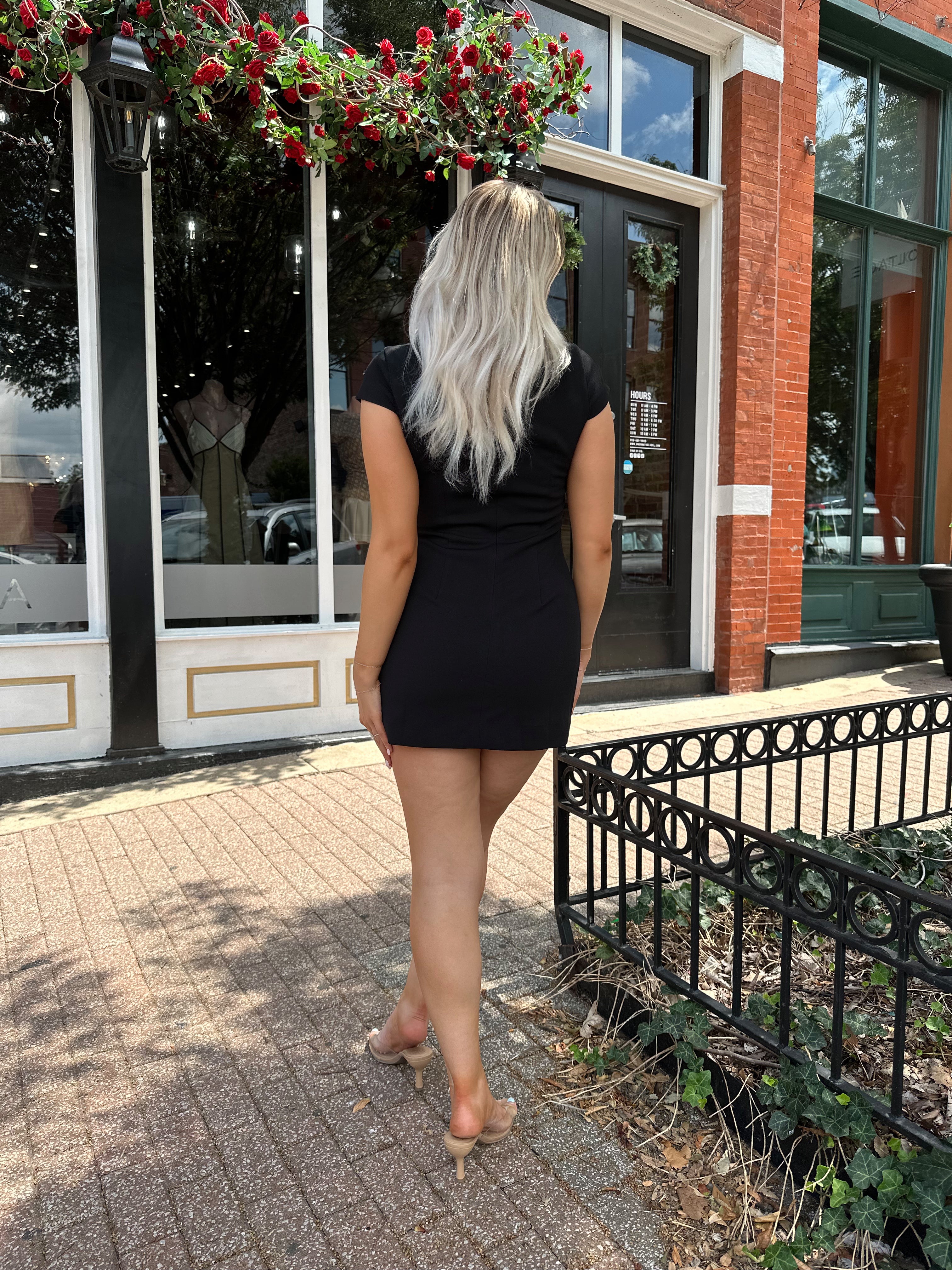 Woman wearing black tailored mini dress with short sleeves and keyhole cutout.
