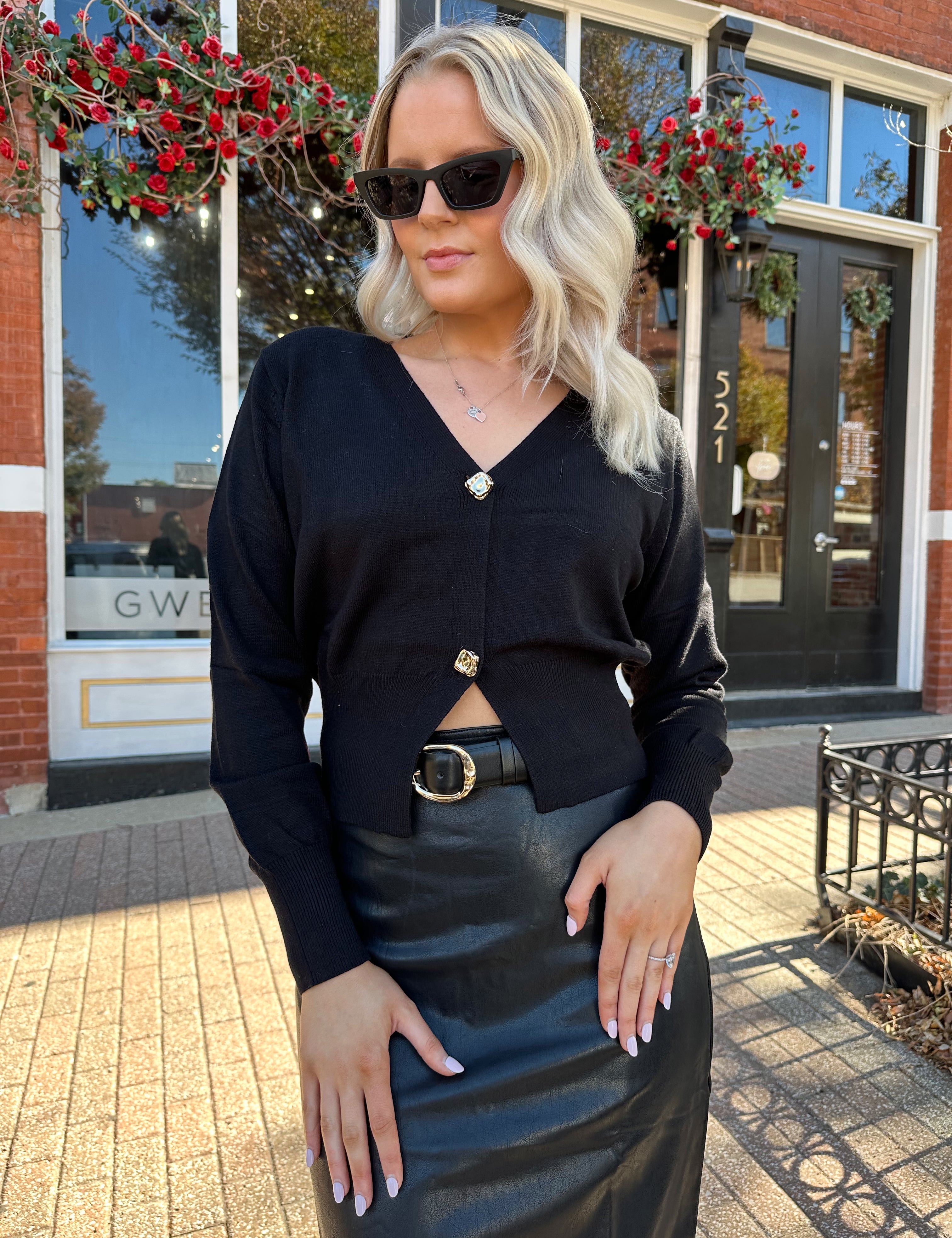 Woman wearing black sweater cardigan with gold button detailing closure, and black leather midi skirt.