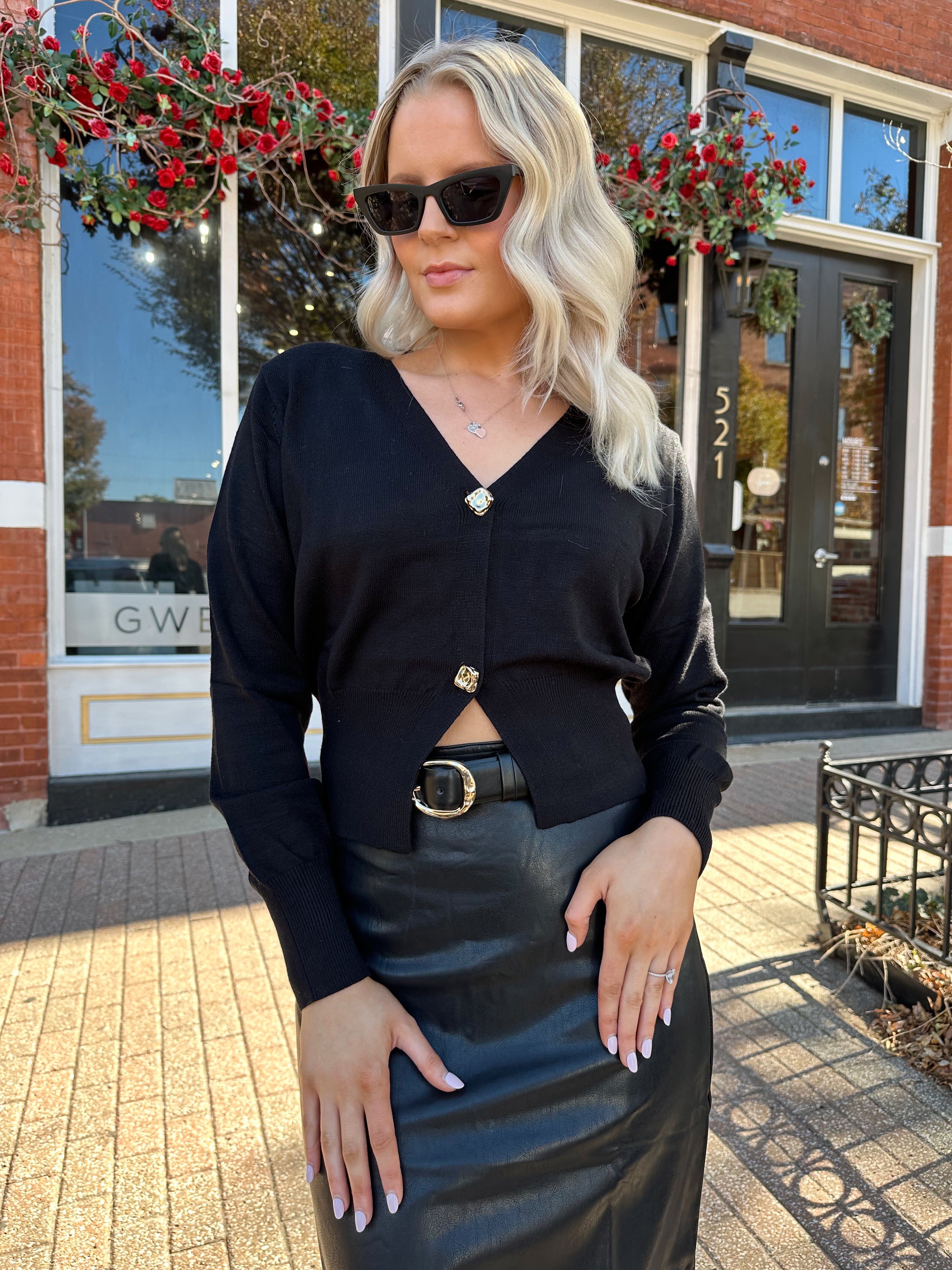 Woman wearing black sweater cardigan with gold button detailing closure, and black leather midi skirt.