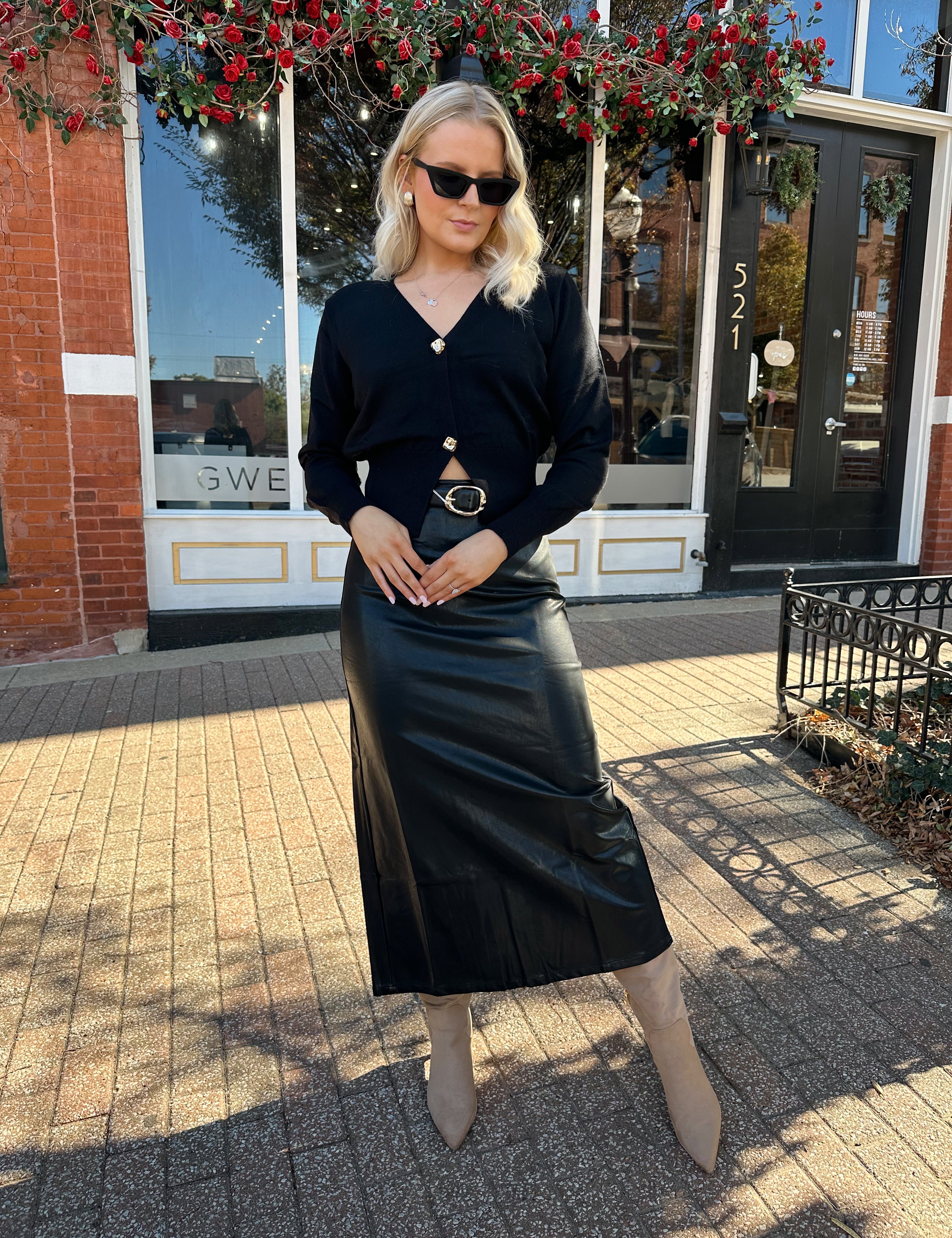Woman wearing black sweater cardigan with gold button detailing closure, and black leather midi skirt.