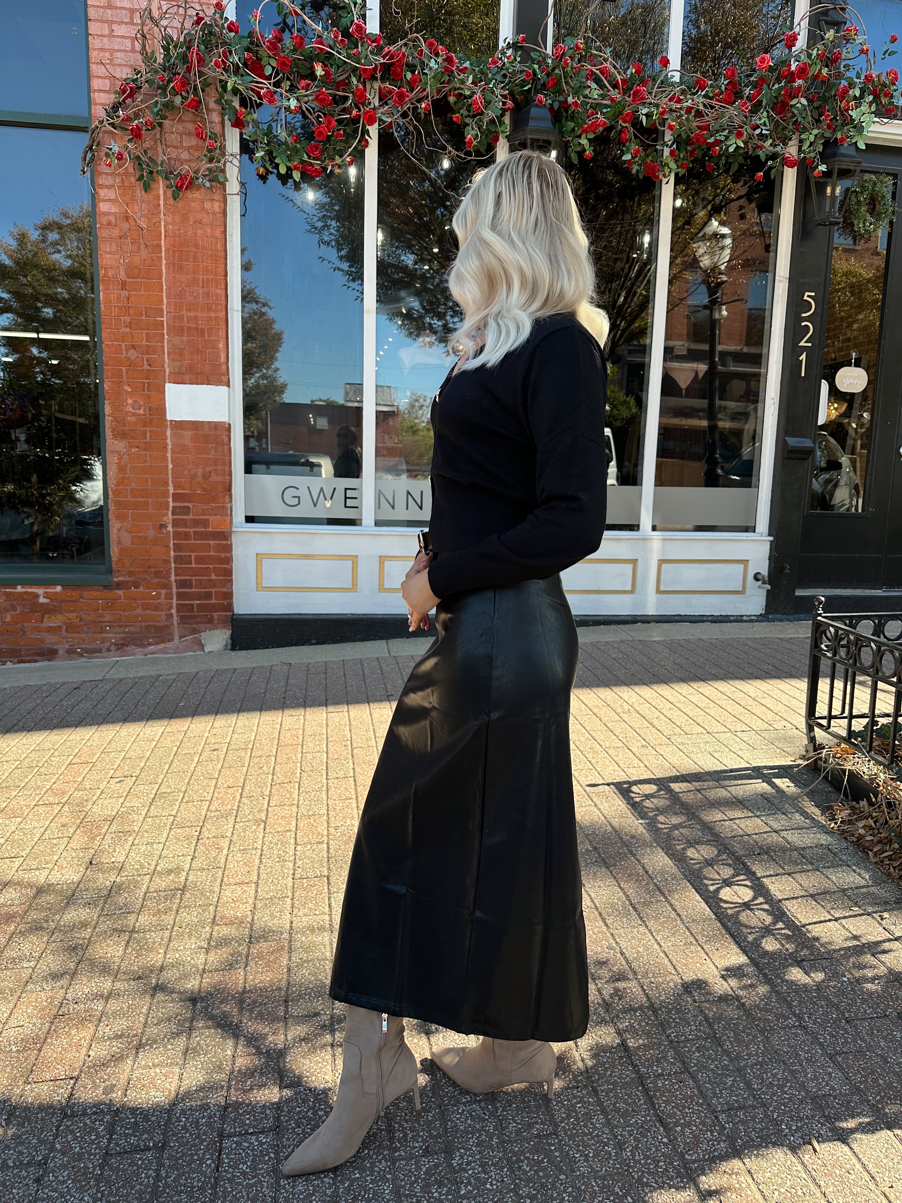 Woman wearing black sweater cardigan with gold button detailing closure, and black leather midi skirt.