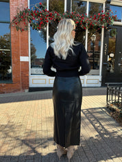 Woman wearing black sweater cardigan with gold button detailing closure, and black leather midi skirt.