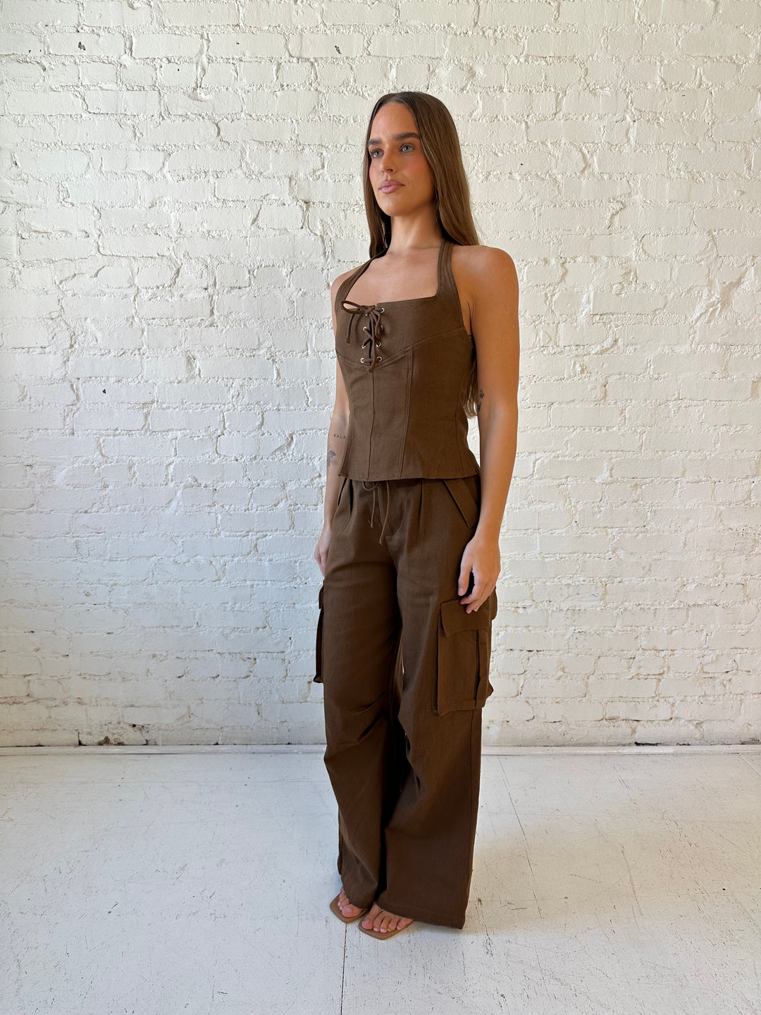 Woman wearing brown two piece cargo pant set with halter neck, and lace up front detail. 