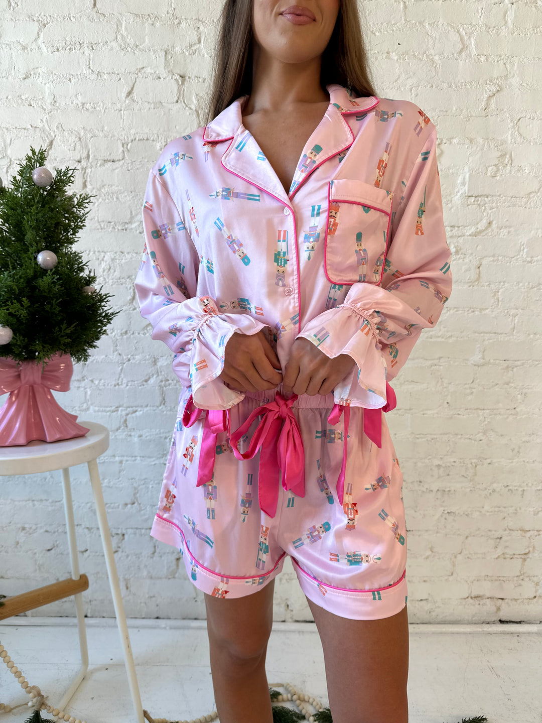 Woman wearing pastel pink satin pajamas with pastel nutcrackers all over. 