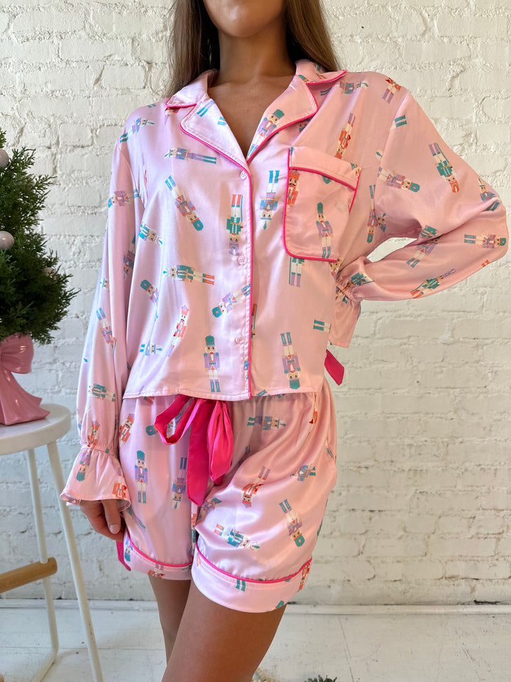 Woman wearing pastel pink satin pajamas with pastel nutcrackers all over. 