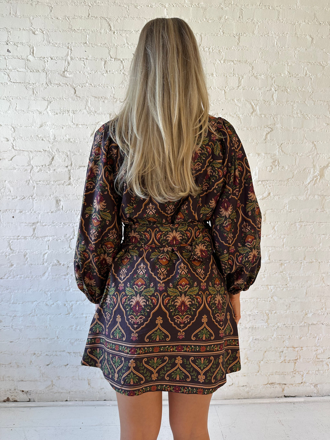 Woman wearing brown pattern long sleeve mini dress with belted waist, and knee cream boots.