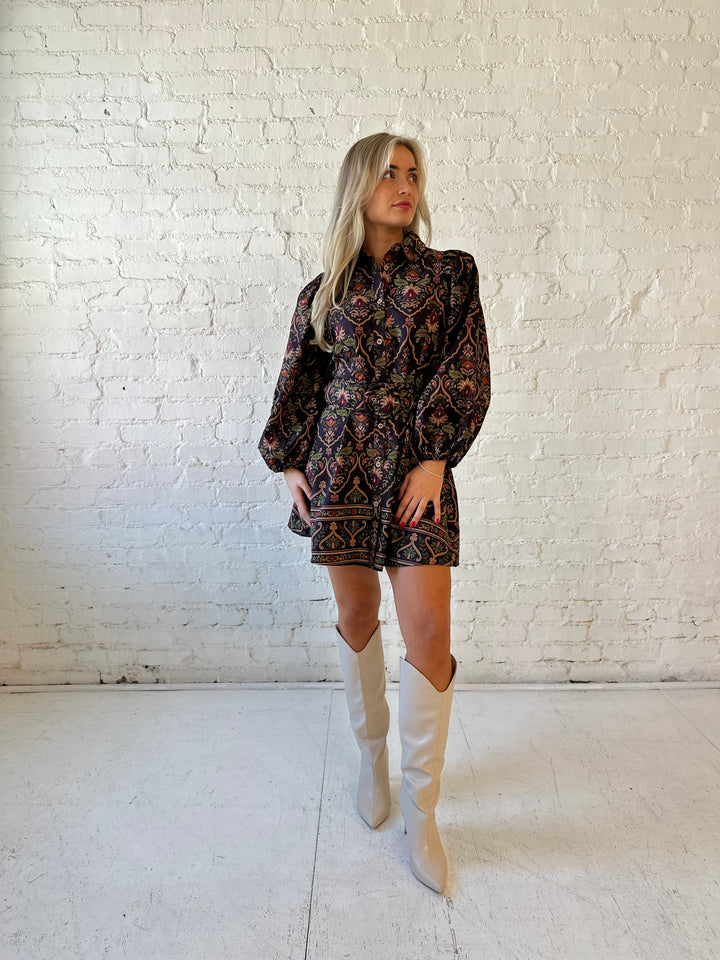 Woman wearing brown pattern long sleeve mini dress with belted waist, and knee cream boots.