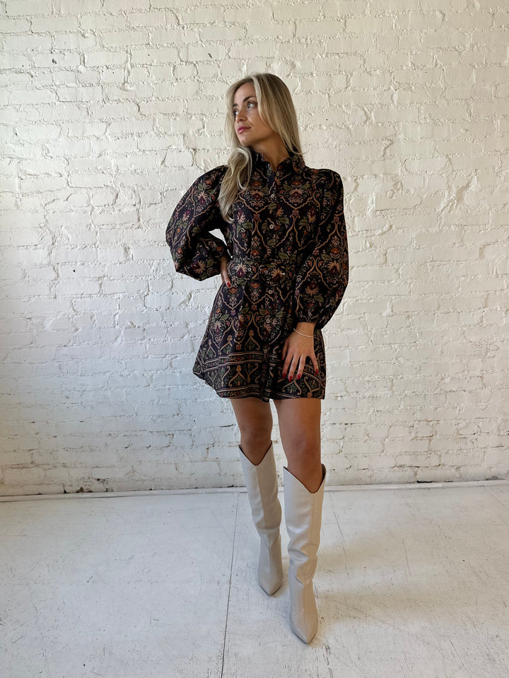 Woman wearing brown pattern long sleeve mini dress with belted waist, and knee cream boots.
