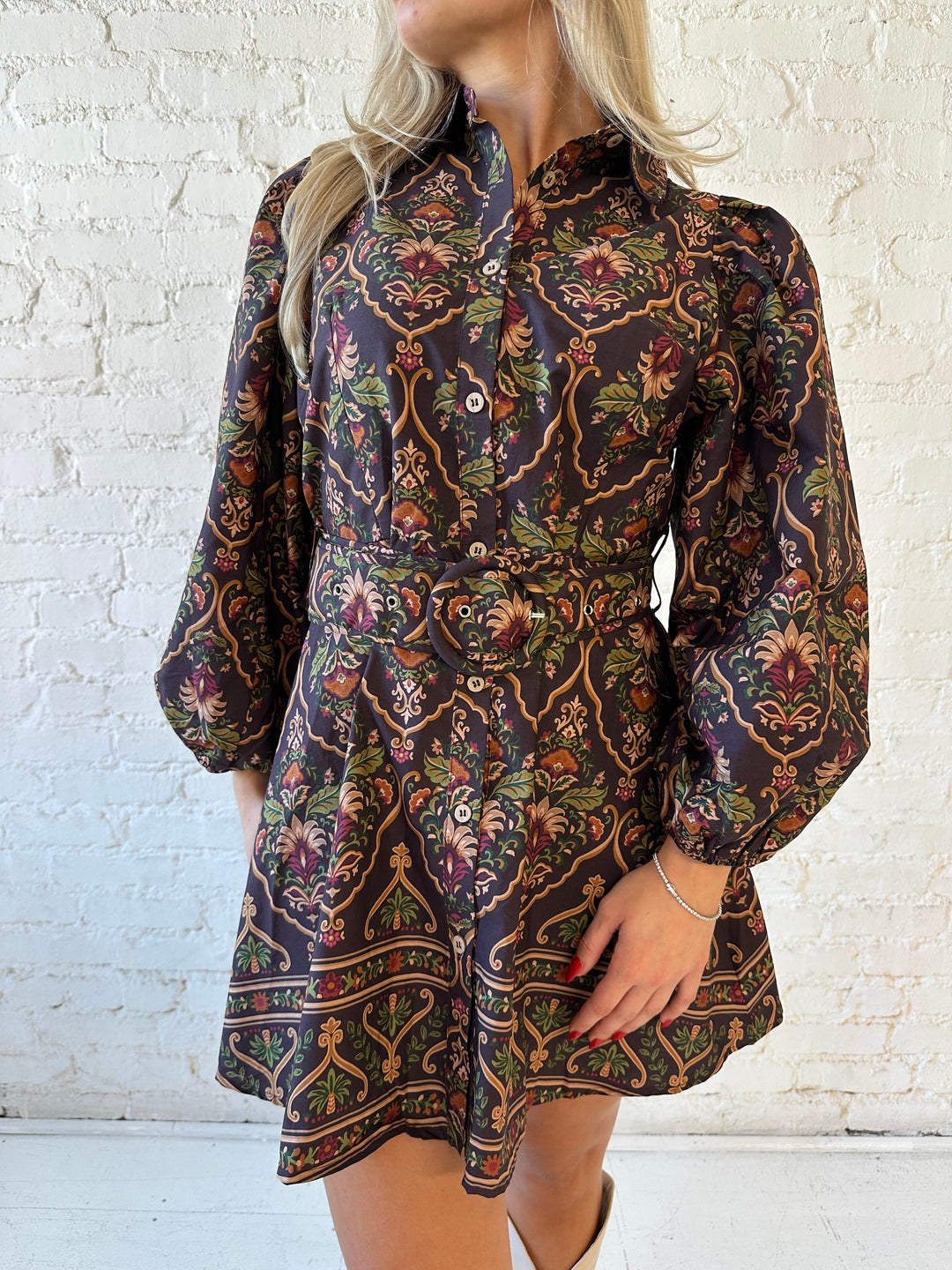 Woman wearing brown pattern long sleeve mini dress with belted waist, and knee cream boots.
