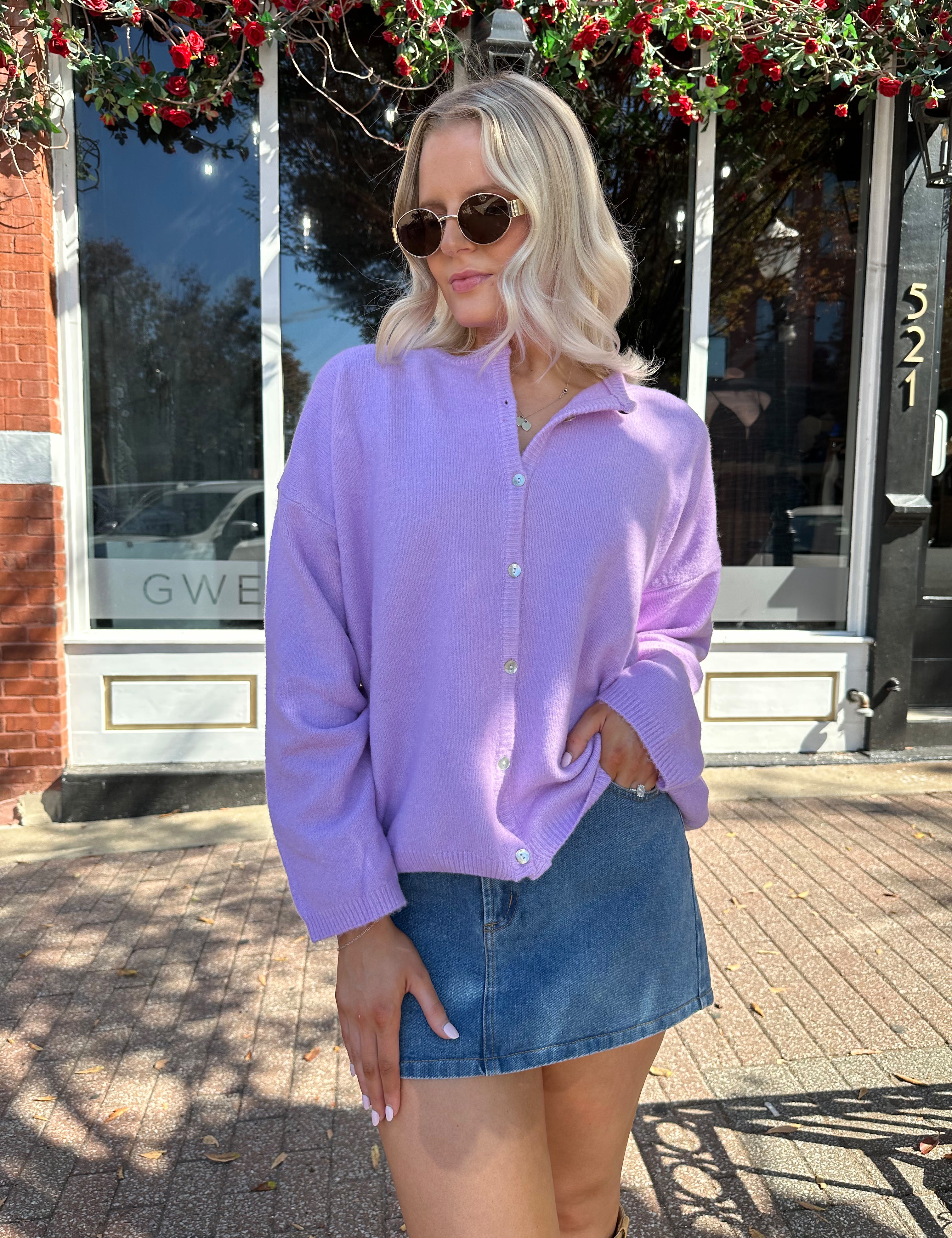 Woman wearing lavender knit button up cardigan with denim skirt. 