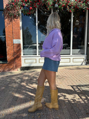 Woman wearing lavender knit button up cardigan with denim skirt. 