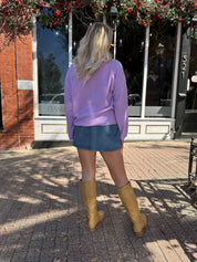 Woman wearing lavender knit button up cardigan with denim skirt. 