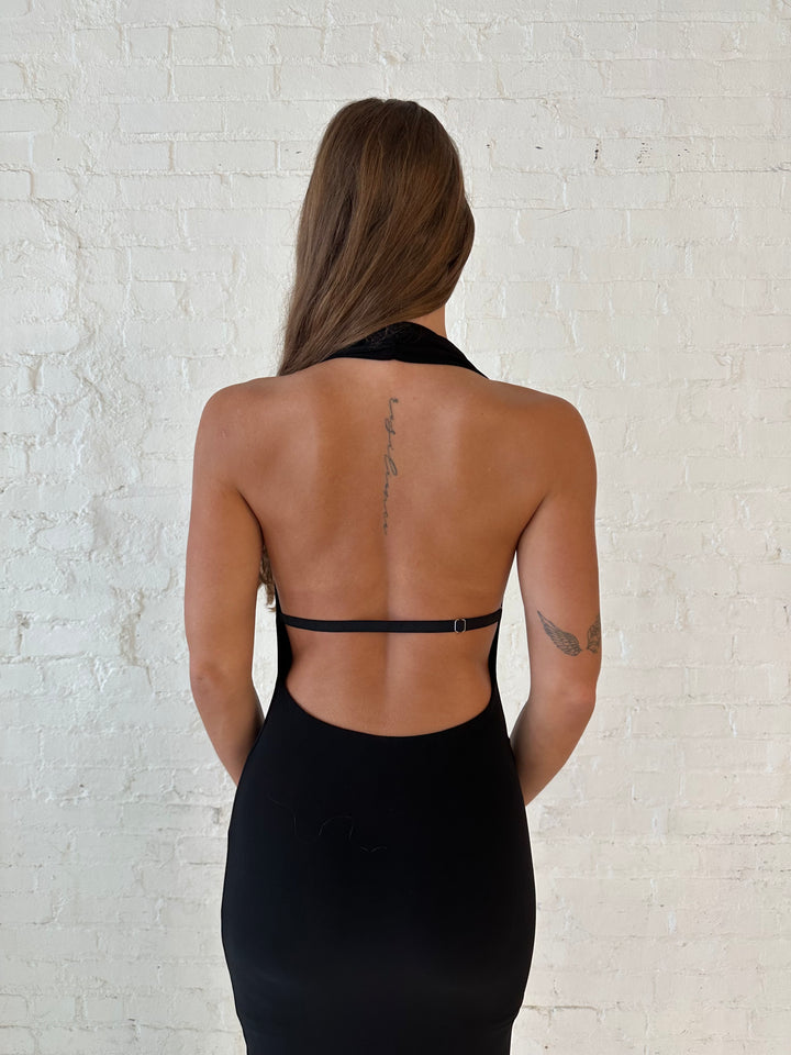 Woman wearing black maxi dress with halter cowl neckline, open back with and strap support.