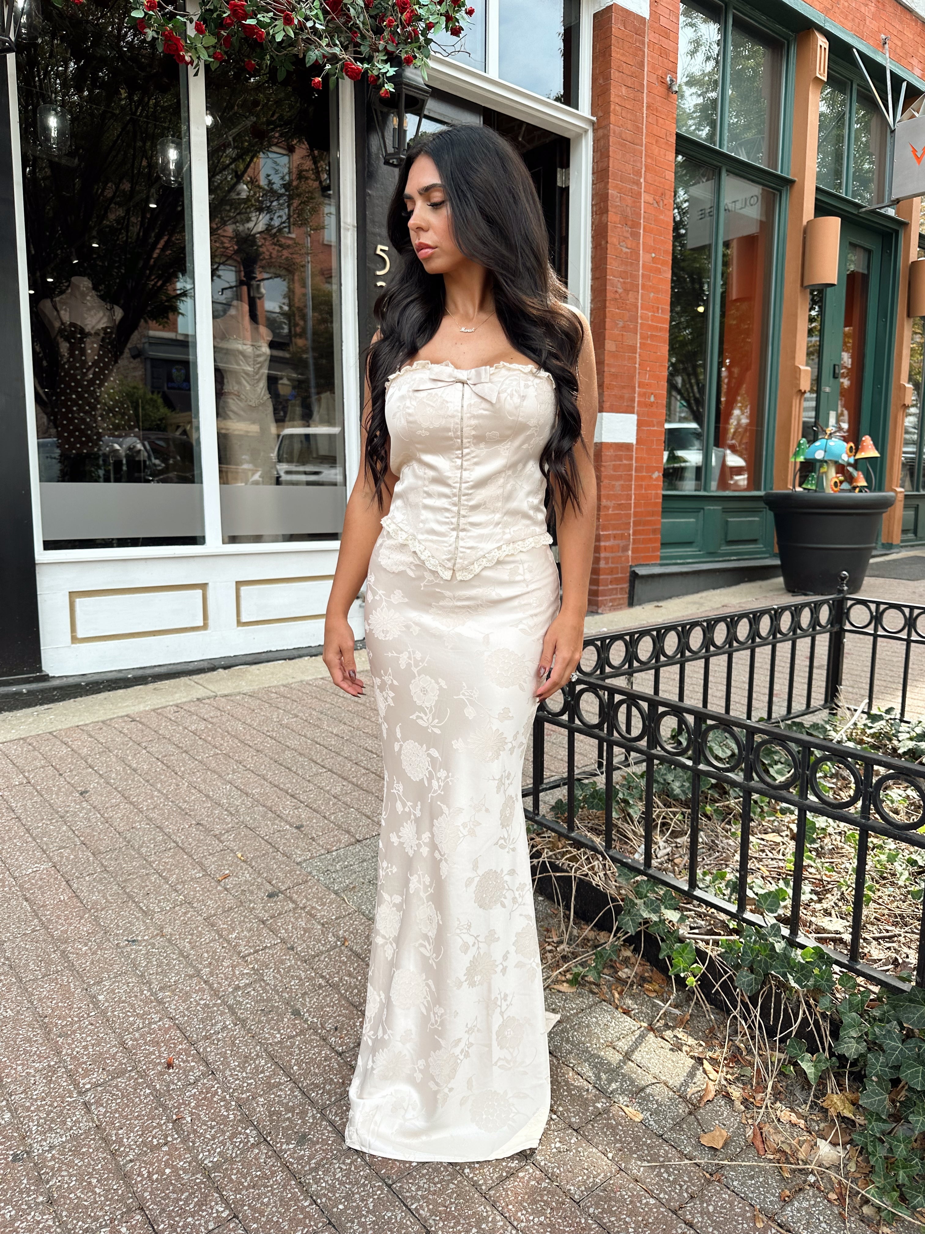 Woman wearing champagne floral satin two piece set with corset top and maxi skirt. 